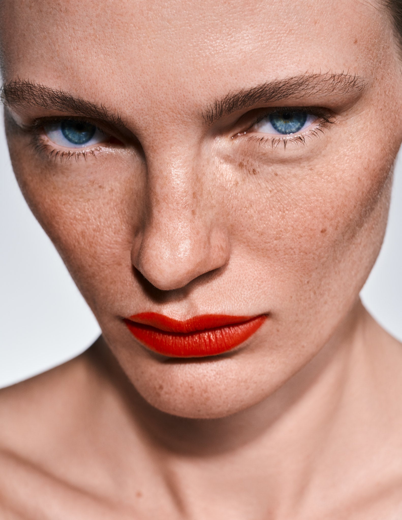 Close-up of a person with blue eyes and red lipstick on a neutral background